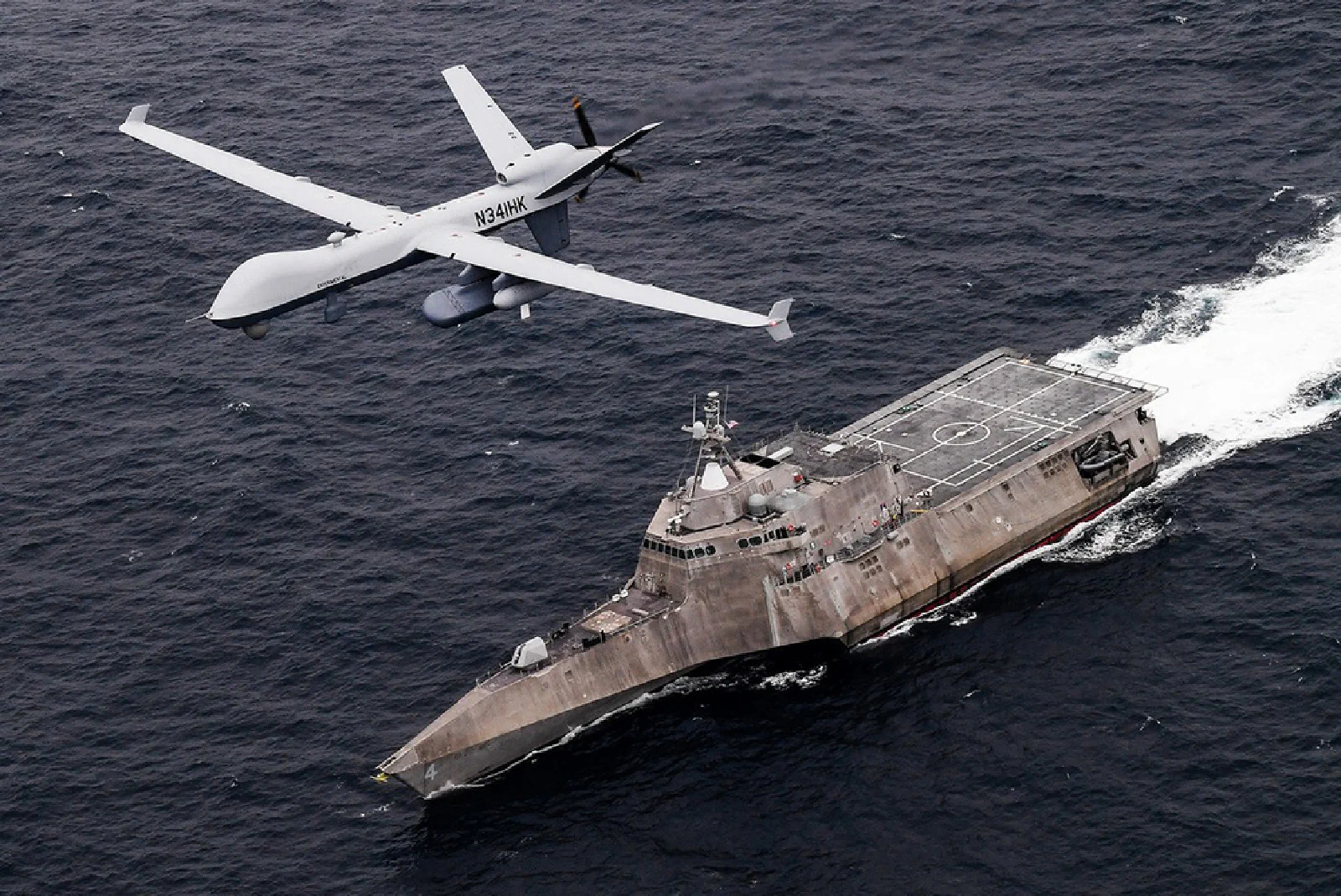 An unmanned aircraft flying beside a Navy ship during Unmanned Integrated Battle Problem 21.